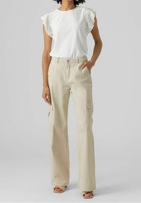 Blusa bianca in pizzo con maniche a volant, abbinata a pantaloni cargo beige chiaro con tasche laterali e una vestibilità comoda. Accentuata da sandali con punta aperta.