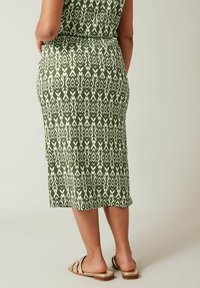 Gonna midi verde con motivo a fantasia e disegni geometrici bianchi, tessuto texturizzato e vita aderente. Abbinata a sandali piatti marroni.