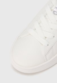 Valge tennisking, millel on sile sünteetiline pealispind, ümar varvas ja lamedad paelad. Sisaldab tekstuuriga detaile ja kummist tallaga.