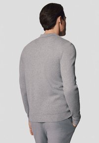 Szary sweter z długim rękawem, gładka dzianina, okrągły dekolt, ściągacze na rękawach i u dołu, lekko dopasowany krój, widoczne detale przeszycia.