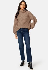 Béžový pletený rolák s pohodlným střihem a texturovaným povrchem, spárovaný s tmavě modrými džíny rovného střihu a černými kotníkovými botami.
