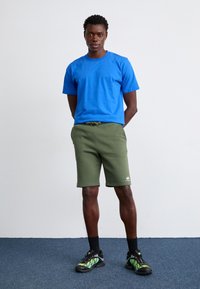 Blå crew neck t-shirt, olivengrønne shorts med elastisk talje og sorte sneakers med grønne accenter. Glat stof, afslappet pasform.