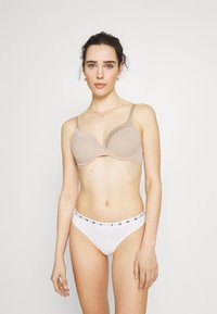 Nude underwire bh med glatte kopper og justerbare stropper, kombinert med hvite bikinitruser med en svart "TOMMY" logo på midjebåndet.
