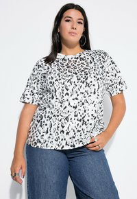Koszulka w print w panterkę w kolorze białym i czarnym, krótki rękaw, okrągły dekolt, miękki materiał, luźny krój, zestawiona z niebieskimi dżinsami.