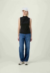 Μαύρο αμάνικο τοπ με ψηλό λαιμό συνδυασμένο με μπλε τζιν ίσιας γραμμής. Ολοκληρώνει το look μία λευκή καμπάνα και ανοιχτόχρωμα αθλητικά παπούτσια.