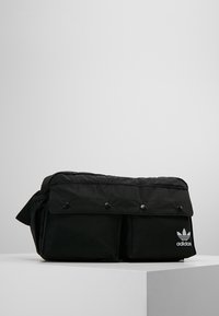 Svart Adidas midjeväska med framklaff och tryckknappar, två framfickor och vitt Adidas-logotyp på nedersta högra fickan.