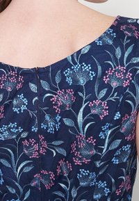 Robe bleu marine ornée de broderies florales dans des tons de rose et de bleu, avec un décolleté en forme de scoop et une fermeture éclair centrée à l'arrière.