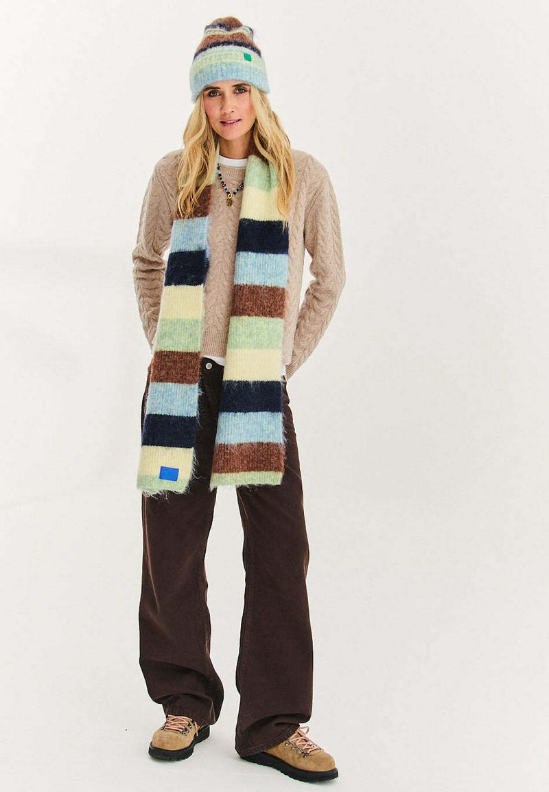 Wielokolorowy dziany szalik w paski w odcieniach niebieskiego, zielonego, brązowego i kremowego. Miękka faktura, prostokątny kształt, z niebieską metką na jednym końcu.