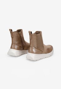 Botas de tobillo sintéticas en color tostado con acabado suave, cremallera lateral y suela de goma blanca. Cuentan con paneles laterales elásticos y tiradores para facilitar su puesta.