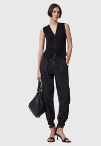 Zwarte geribbelde mouwloze top met een V-hals en knoopsluiting, gecombineerd met hoge zwarte cargobroeken en zwarte sandalen met bandjes.