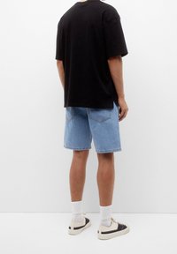 Černé oversize tričko, světle modré džíny šortky, bílé kotníkové ponožky a béžové tenisky s černými akcenty. Jednoduchý design, každodenní střih.