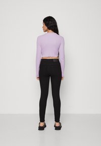 Lila hosszú ujjú crop top és fekete, magas derekú skinny farmer. A farmer hátsó zsebekkel rendelkezik és sima textúrájú.