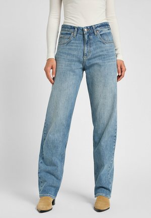 Vaqueros de mezclilla de un azul claro, de pierna ancha y cintura alta, con diseño de cinco bolsillos y detalles de costura. Combinados con botas de tobillo beige.