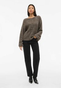 Pull en maille marron avec un col large et des manches surdimensionnées, associé à un pantalon noir droit et des bottines noires.