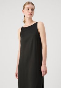 Rochie neagră fără mâneci, cu o textură netedă, siluetă dreaptă și elastice laterale, având un decolteu rotunjit și un design minimal.