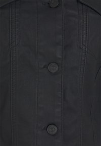 Chaqueta de tela negra que presenta un cierre frontal con botones, cinco botones redondos, costuras detalladas y un cuello estructurado. Superficie texturizada.