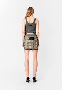 Top sin mangas gris combinado con una falda beige con capas y estampados que presenta acentos negros y bolsillos visibles. La modelo lleva tacones negros.
