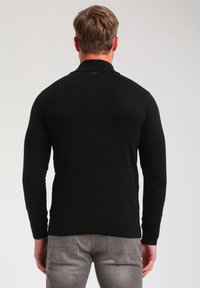 Mustapaitainen neulepusero, jossa on pystykaulus ja pitkät hihat. Kangas näyttää sileältä ja siinä on vartalonmyötäinen muotoilu, nähtynä takaa.