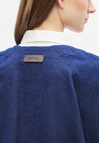 Μπλε τζιν μπουφάν της ναυτικής σχολής με δερμάτινη ετικέτα που φέρει την επωνυμία «Barbour». Διαθέτει κλασι�κό γιακά και δομημένους ώμους με λεία υφή.