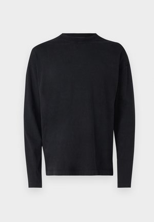 Chemise noire à manches longues en tissu doux. Présente un col rond et des épaules tombantes. Texture lisse sans motifs visibles.