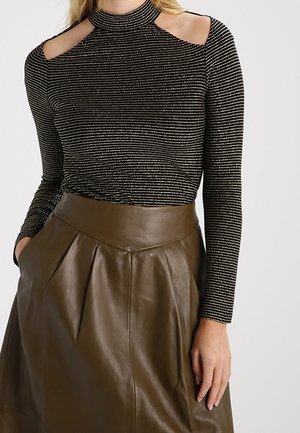 Zwart- en zilvergestreept top met lange mouwen en cut-out schouders, gecombineerd met een hoge taille bruin leren rok met plooien.