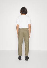 Spodnie bawełniane w kolorze oliwkowej zieleni o prostych nogawkach, z podwiniętymi mankietami i tylnymi kieszeniami, zestawione z gładką białą koszulką. Widoczne czarne buty.