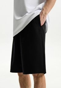 Black shorts with a smooth texture, side pockets, and a simple design, paired with a white t-shirt partially covering the waistband.