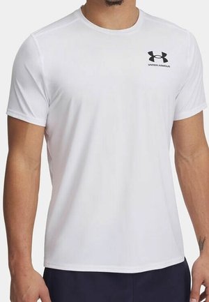 Mężczyzna ubrany w prosty biały t-shirt Under Armour z krótkim rękawem i logo na lewej piersi, w połączeniu z ciemnymi szortami.