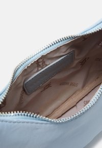 Interno di una borsa in pelle azzurro chiaro con chiusura a zip, dotato di una fodera beige semplice e una piccola tasca, impreziosita da motivi a logo in rilievo.