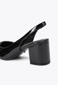 Czarne patentowe obuwie na obcasie z odkrytymi piętami i grubym kwadratowym obcasem. Gładka tekstura i minimalistyczny design z metalowymi akcentami z tyłu.