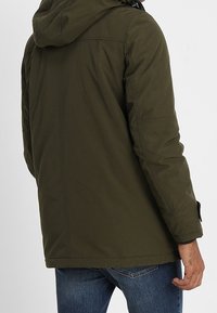 Olivgrön, huva jacka med en slät textur, med rak passform, sydda detaljer och justerbara ärmslut. Inga synliga logotyper.