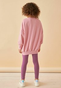 Rosa oversized tröja med puffärmar, tillsammans med lila leggings och vita sneakers med iriserande detaljer.