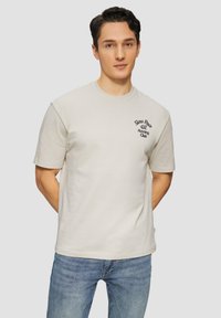 Lichtbeige katoenen T-shirt met korte mouwen en een ronde halslijn, met marineblauwe geborduurde tekst die zegt "Slow Pace Running Club."