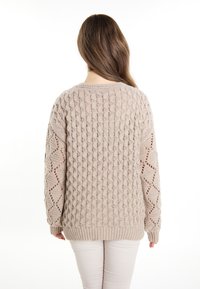 Maglione beige lavorato a maglia con un motivo testurizzato, caratterizzato da disegni a traforato sulle maniche. Le maniche a costine e l'orlo aggiungono dettagli.