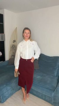 Hvit bluse med broderte blomsterdetaljer, kombinert med et burgunderfarget kordfløyelskjørt med splitt foran. Brune hæler og en clutch fullfører antrekket.