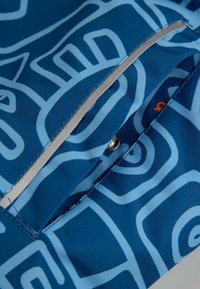 Niebieska tkanina z jasnoniebieskim abstrakcyjnym wzorem, z zapięciem na zatrzask i srebrnym akcentem wzdłuż krawędzi kieszeni.