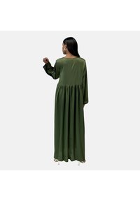 Lang, flydende maxikjole i mørkegrønt stof. Har en rund halsudskæring, lange ærmer og en indsamlet talje for ekstra volumen.