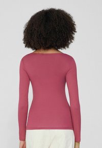 Langärmliges, eng anliegendes Rippoberteil in rosarot. Mit weitem Ausschnitt und glatter Textur. Rückansicht, die das figurschmeichelnde Design zeigt.