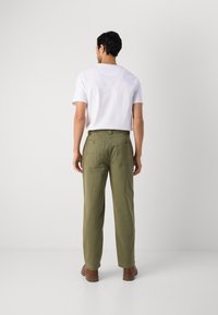 Olive green relaxed-fit trousers with back pockets, paired with a white t-shirt. Pants have a smooth texture and straight leg design.