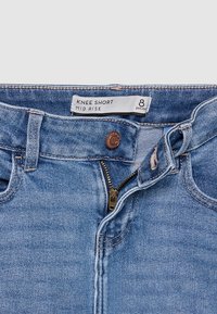 Short en denim bleu bleu mi-haut à hauteur du genou avec fermeture éclair partiellement ouverte et bouton fermé, taille 8 petite, étiquette visible à l'intérieur de la ceinture.