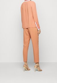 Blusa pesca con un colletto rifinito in bianco e rosso, abbinata a pantaloni tapered coordinati. Il materiale sembra liscio; accentuata con sandali con tacco dorato.