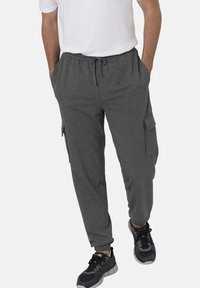 Graue Baumwoll-Cargo-Hosen mit elastischem Bund und Kordelzug, ausgestattet mit seitlichen Taschen und einer schmal zulaufenden Beinform. Getragen mit schwarzen Sneakers.