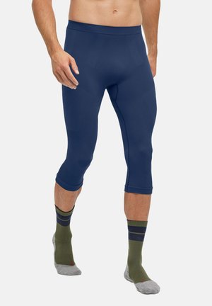 Pantalons capri de sport bleu marine en matériau extensible, avec des accents texturés et une coupe ajustée, associés à des chaussettes de crew à rayures vertes.