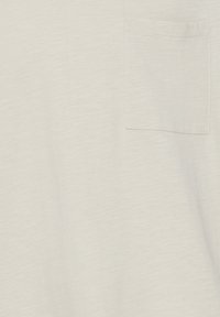 Lys beige kortærmet t-shirt lavet af blødt stof, med en lille lomme på venstre bryst og en let tekstureret overflade.