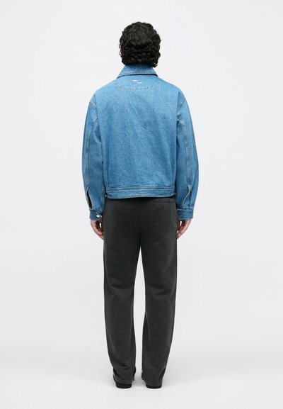 Kék farmerdzseki klasszikus szabással, hegyes gallérral és látható varrással, sötétszürke nadrággal és fekete cipővel párosítva.