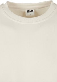 Šviesiai smėlio spalvos organinės medvilnės džemperis su tekstūruotu, gofrais pasiūtu apvaliu kaklu ir tiesiu kirpimu. Etiketėje užrašas „Urban Classics“, dydis M.