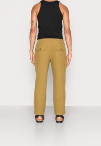 Pantaloni in misto lino verde oliva con due tasche posteriori e vestibilità dritta, indossati con un top nero senza maniche e sandali.