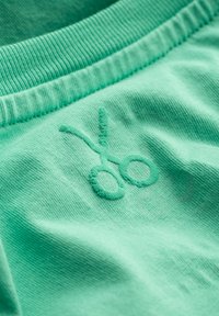 Tessuto verde menta con ricamo testurizzato a forma di forbici, dotato di una cintura a costine e sfondo liscio.