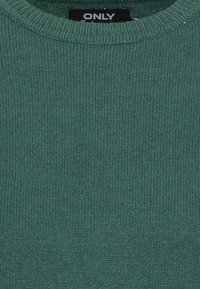 Grön stickad tröja med rund halsringning och ribbad textur. Har en etikett som visar märket "ONLY" vid halsområdet.