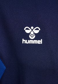 Mörkblå sporttröja gjord av texturerad tyg, med en vit Hummel-logotyp och en blå diamantaccent på vänster sida.